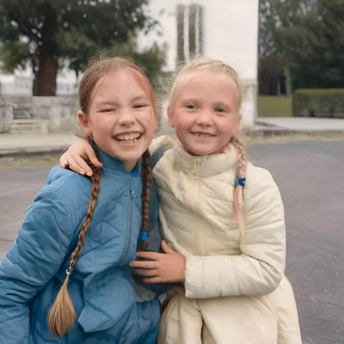 Two young girls smiling and hugging outdoors,