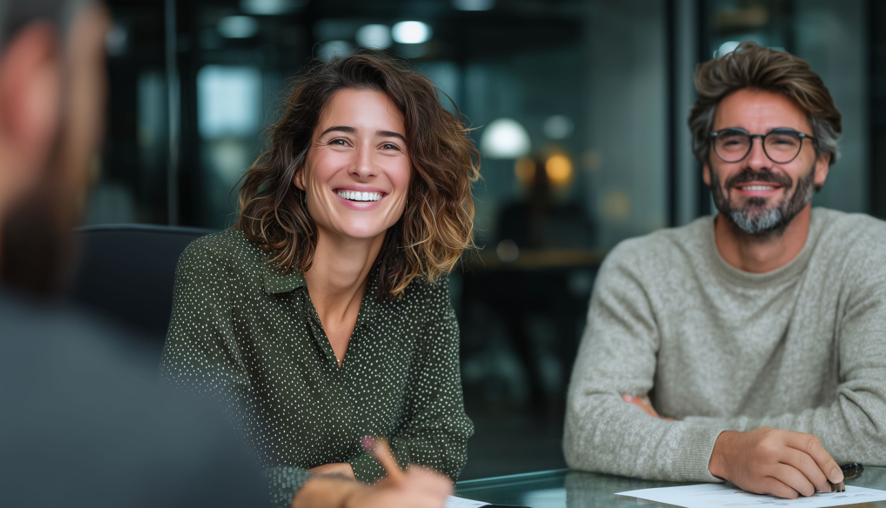 Smiling couple sitting across a desk from an advisor in a modern office setting