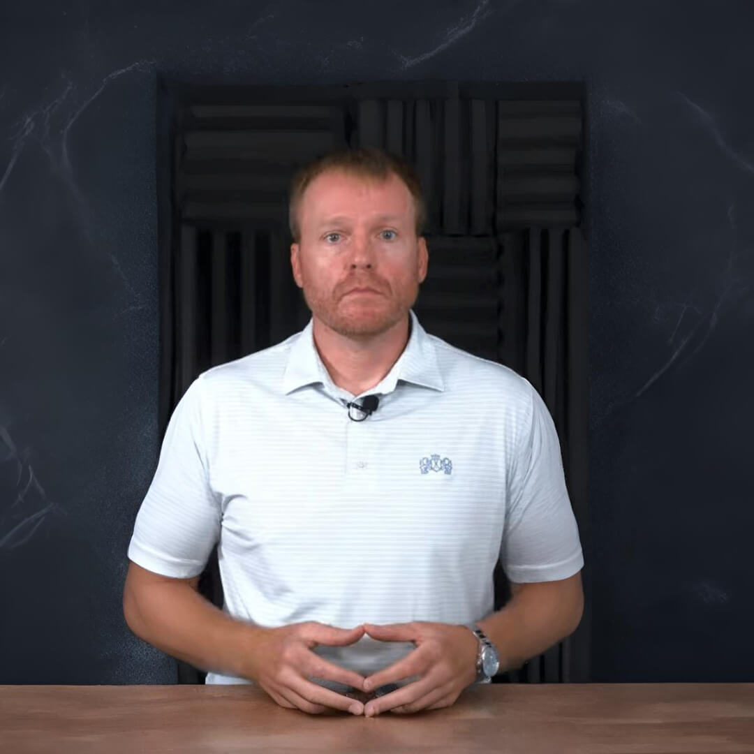 Chris Kelly in a light polo shirt sitting at a desk